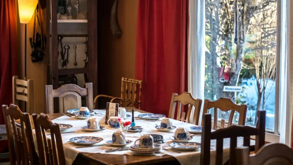 Sala de jantar rústica e acolhedora em pousada na Patagônia, com mesa posta para café da manhã e vista para o jardim.