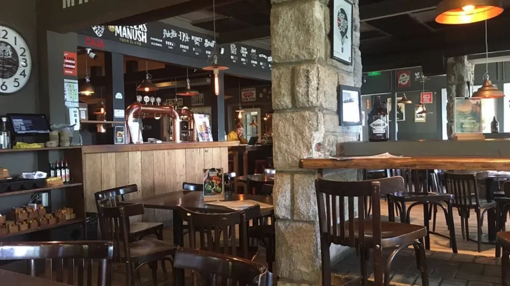 Interior da Manush com balcão de madeira, torneiras de chope e mesas de madeira.