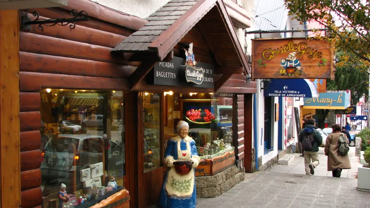Entrada charmosa da loja Abuela Goye em Bariloche, com fachada de madeira e estátua de vovó segurando chocolate na calçada.