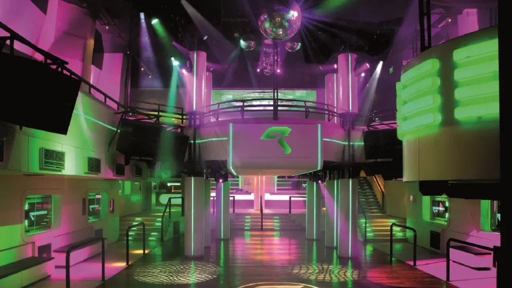Interior iluminado da discoteca Genux em Bariloche, com pista de dança vazia, luzes de neon verde e rosa, e globo espelhado no teto.