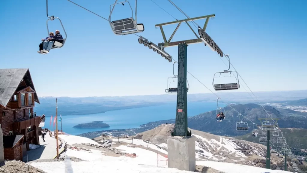 Vista panorâmica do Cerro Catedral em Bariloche, com teleférico, neve nas montanhas e o lago Nahuel Huapi ao fundo.