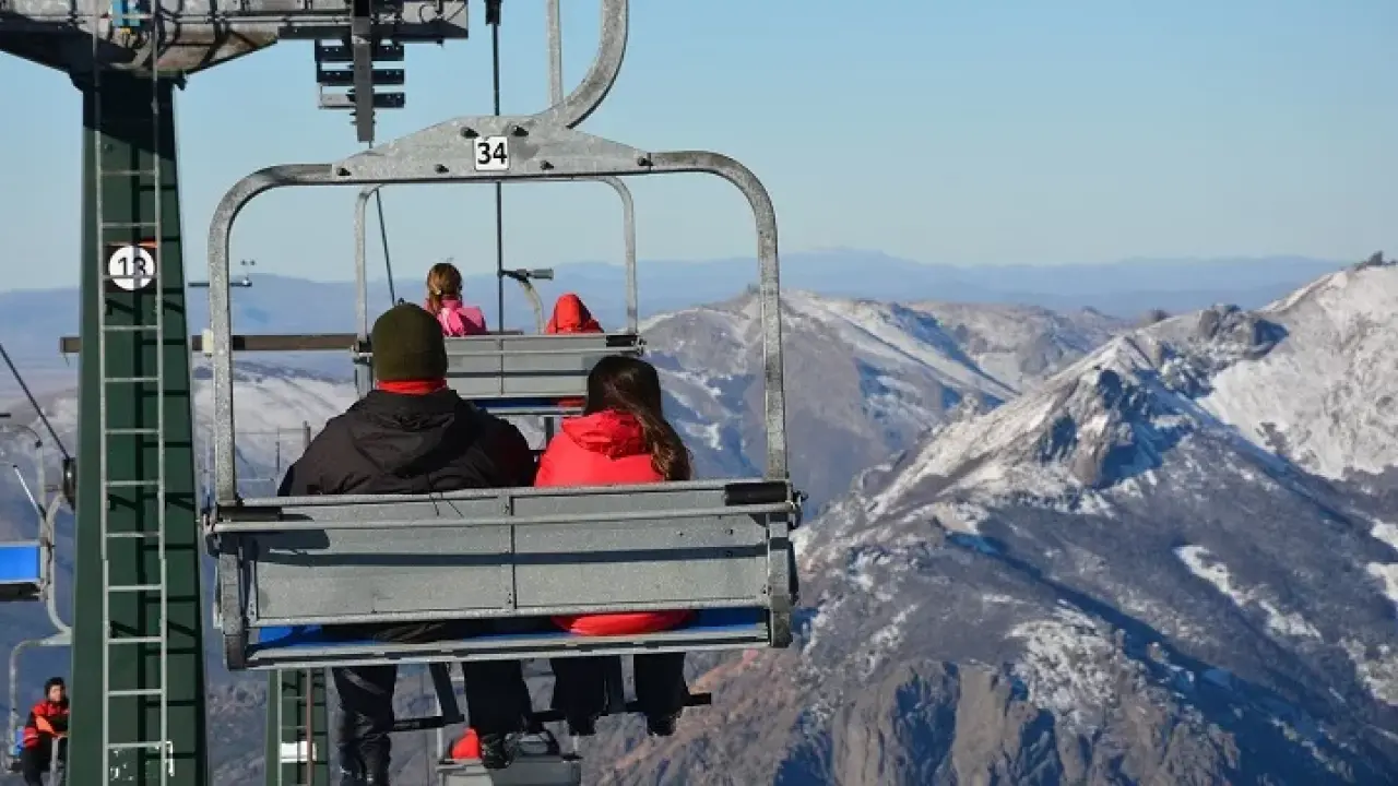Turistas usando roupas de neve em teleférico no Cerro Catedral, com montanhas nevadas ao fundo durante o inverno em Bariloche.