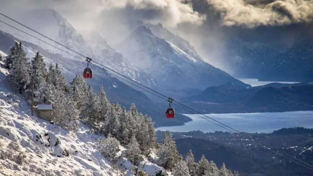 Teleférico sobre as montanhas nevadas de Cerro Catedral, com vista para os lagos e florestas de Bariloche, em um dia nublado.