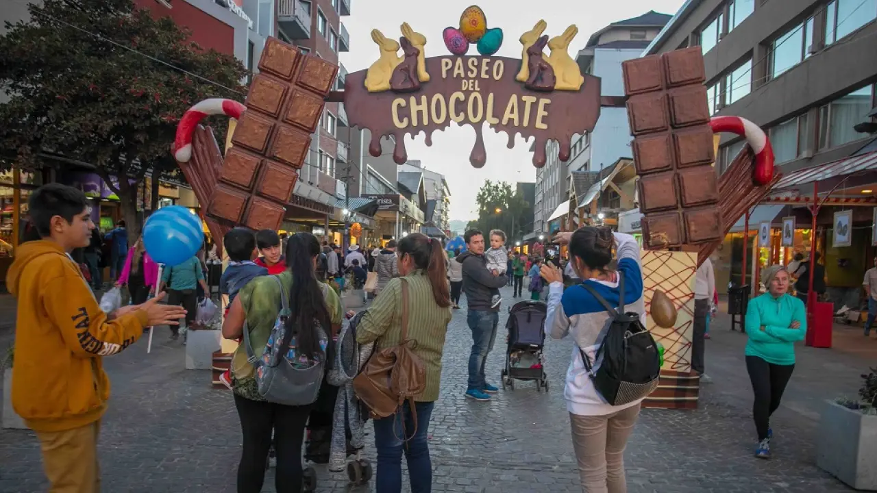 Entrada temática do Paseo del Chocolate na Calle Mitre, em Bariloche, com turistas caminhando entre lojas e decoração de chocolate gigante.