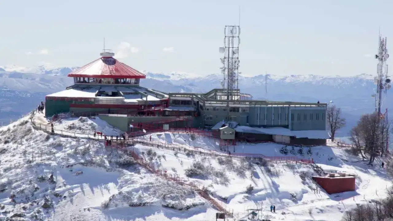 Cerro coberto de neve com estruturas de observação e torres de comunicação no topo da montanha em Bariloche.