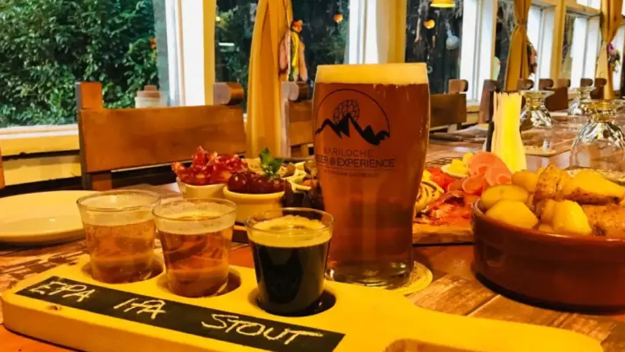 Régua de degustação de cervejas artesanais com as variedades EPA, IPA e Stout, ao lado de um copo de cerveja e uma tábua de frios em uma cervejaria.