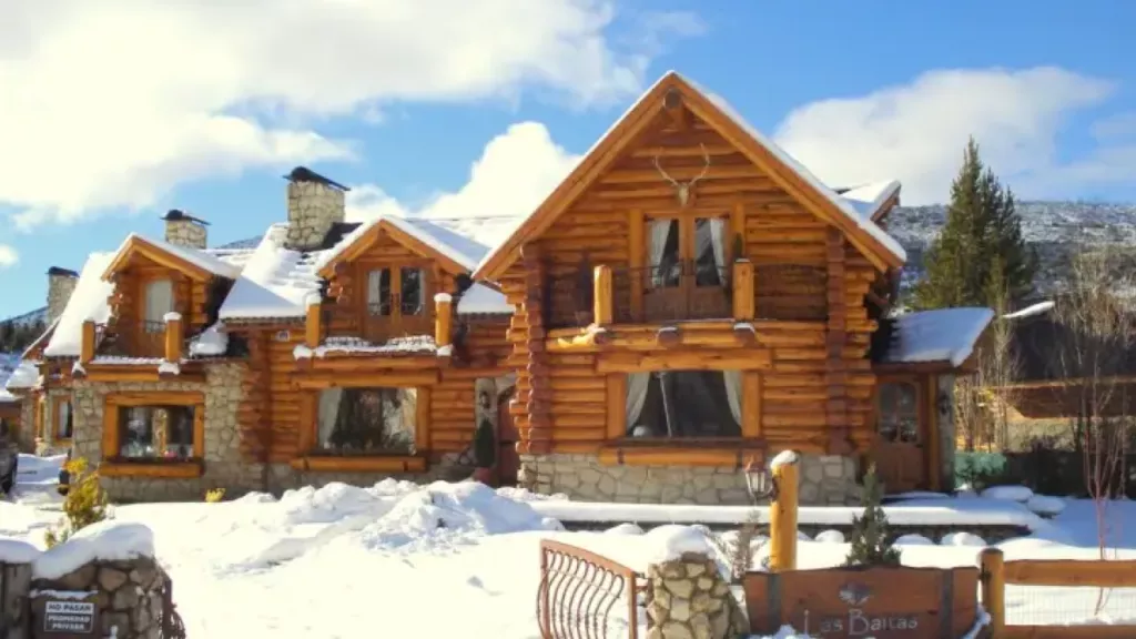 Cabana rústica de madeira com arquitetura alpina, cercada por neve, em um cenário invernal de Bariloche.