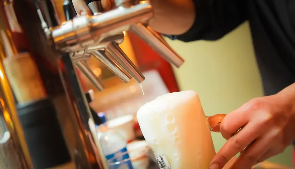 Chopeira servindo uma cerveja gelada em um pub de Bariloche, com a espuma transbordando do copo.