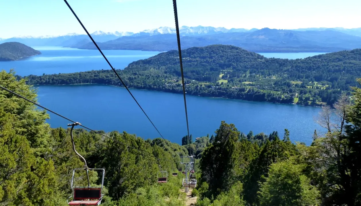 Vista panorâmica do lago Nahuel Huapi em Bariloche, visto de um teleférico cercado por montanhas e florestas verdes.