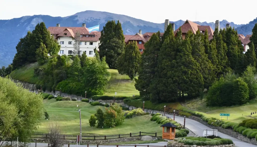 Vista panorâmica de um hotel rodeado por árvores verdes e montanhas ao fundo, representando o cenário da Semana Musical Llao Llao em Bariloche, um evento cultural com apresentações musicais em um ambiente natural deslumbrante.