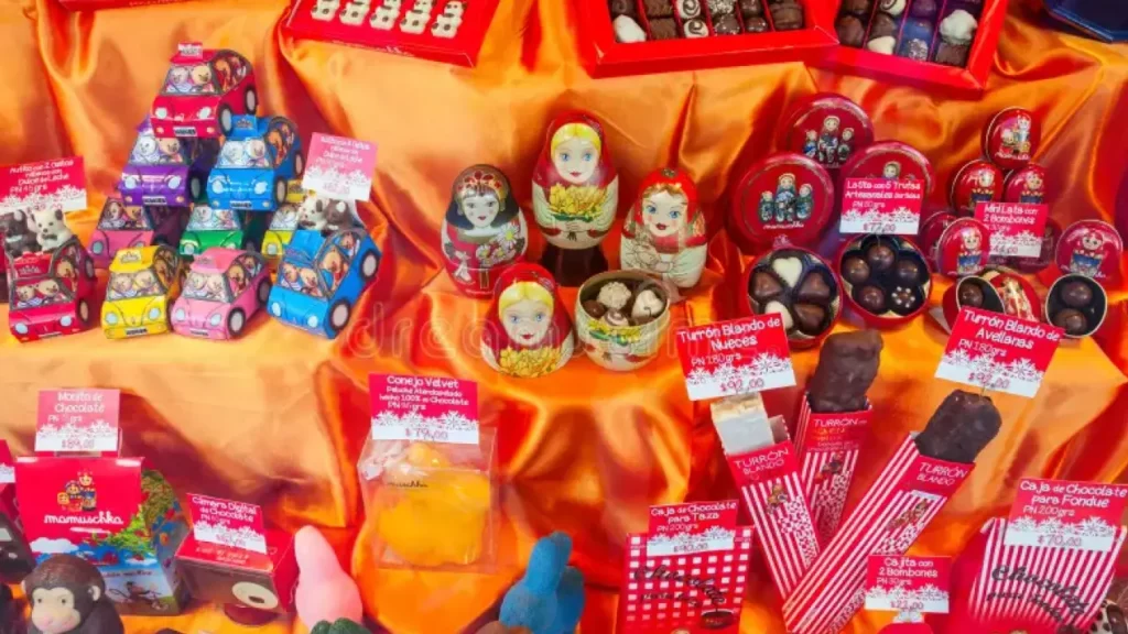 Vitrine colorida da chocolateria Mamuschka com bonecas russas, chocolates artesanais e embalagens decorativas sobre tecido laranja brilhante.