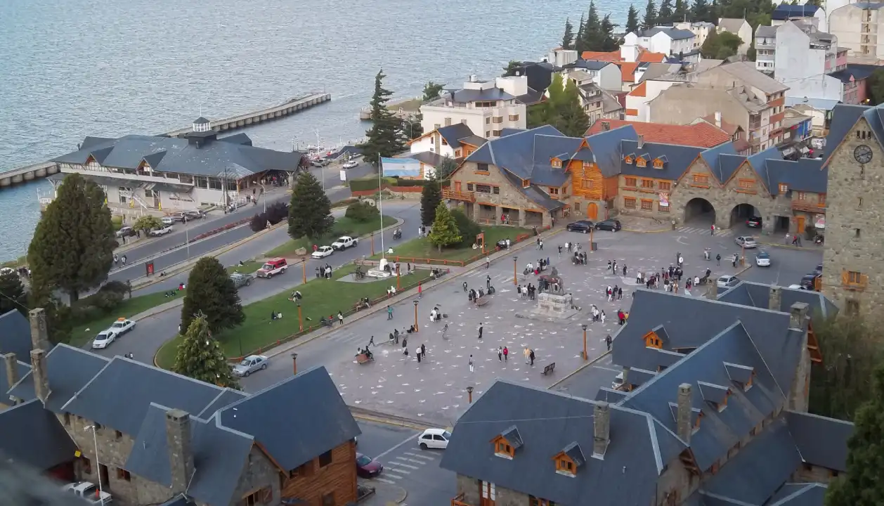 Vista aérea da Praça Principal no Centro Cívico de Bariloche, com edifícios históricos e o Lago Nahuel Huapi ao fundo.