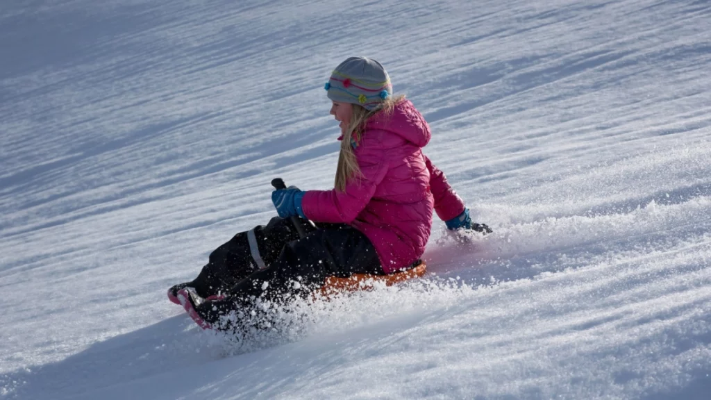 Criança deslizando na neve em uma prancha no parque de inverno Piedras Blancas, Bariloche, Argentina. Diversão e aventura em meio a um cenário de montanhas cobertas de neve.