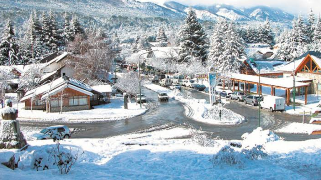 Centro de Villa La Angostura no inverno, com neve cobrindo casas, árvores e ruas da cidade.