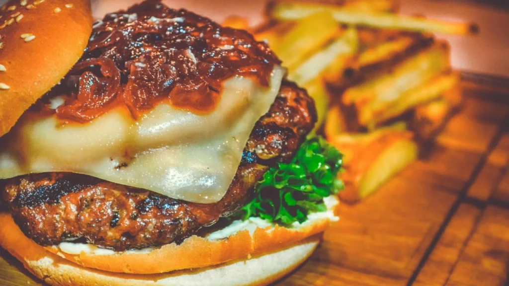 Hambúrguer artesanal com queijo derretido e cebola caramelizada, acompanhado de batatas fritas crocantes.