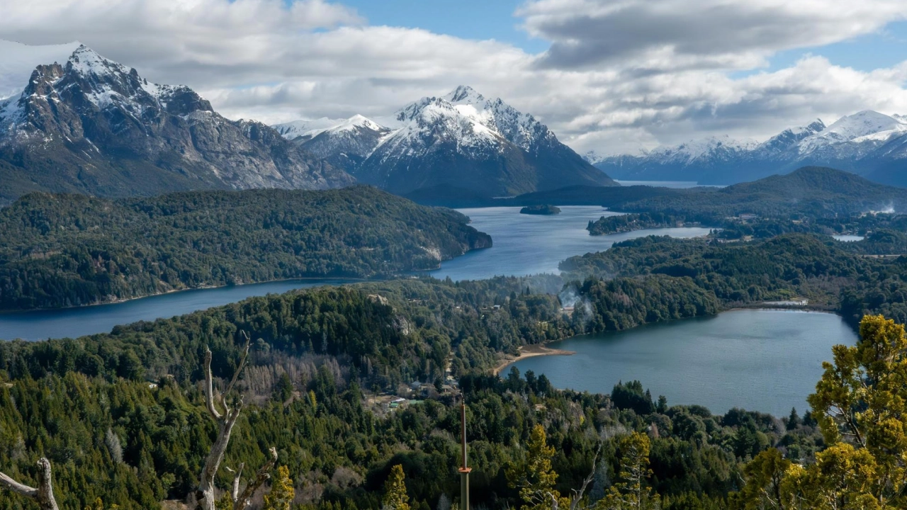 Lagos e montanhas cobertos de neve com vegetação densa em Bariloche, em um dia parcialmente nublado.