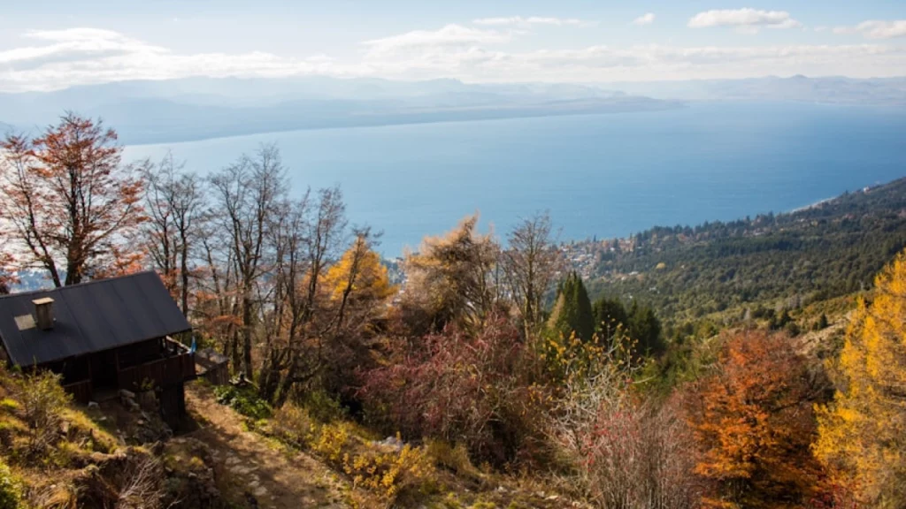 Cabana rústica com vista para o lago cercada por árvores de outono, em uma colina nas montanhas de Bariloche.