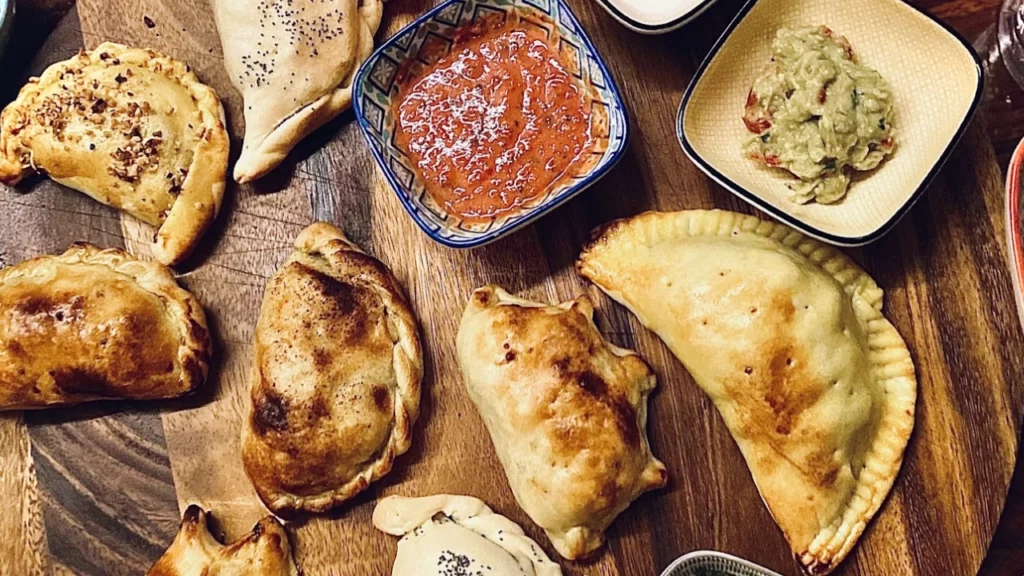 Prato de empanadas argentinas servido com diferentes molhos em pequenos potes, capturando uma típica experiência gastronômica na Argentina.