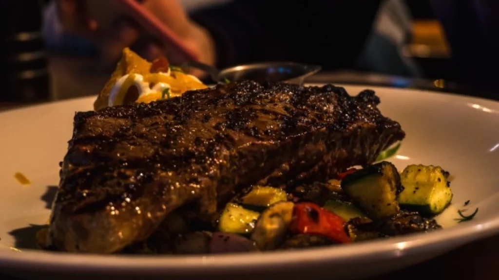 Filé de carne grelhada acompanhado de vegetais assados, pronto para ser servido em um ambiente acolhedor.