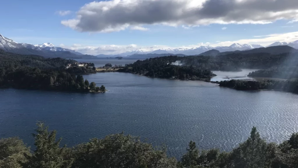 Vista panorâmica do Lago Nahuel Huapi cercado por montanhas com picos nevados em um dia claro e ensolarado em Bariloche.