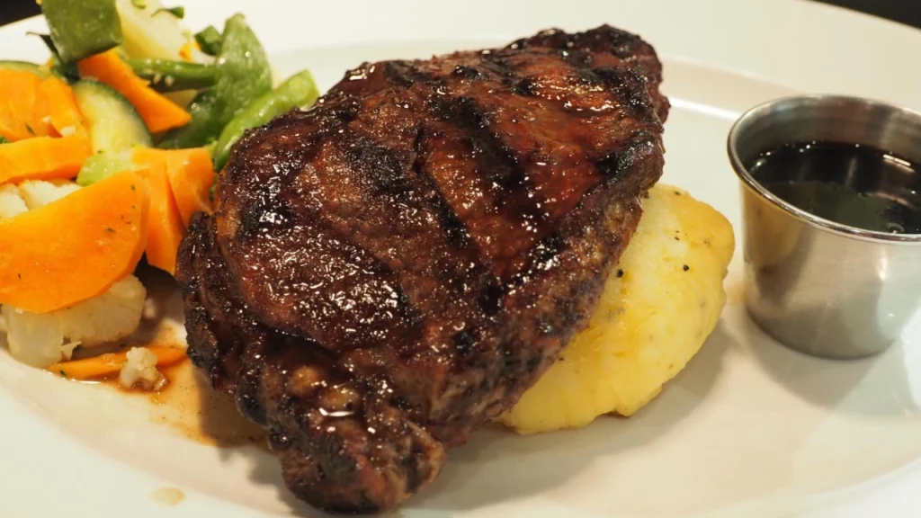 Corte de carne grelhada acompanhado de purê de batatas, legumes frescos e molho à parte.