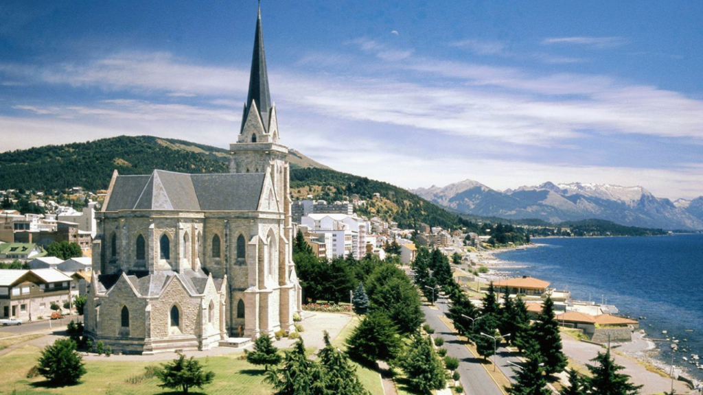 Catedral de Bariloche à beira do lago Nahuel Huapi, com montanhas ao fundo.