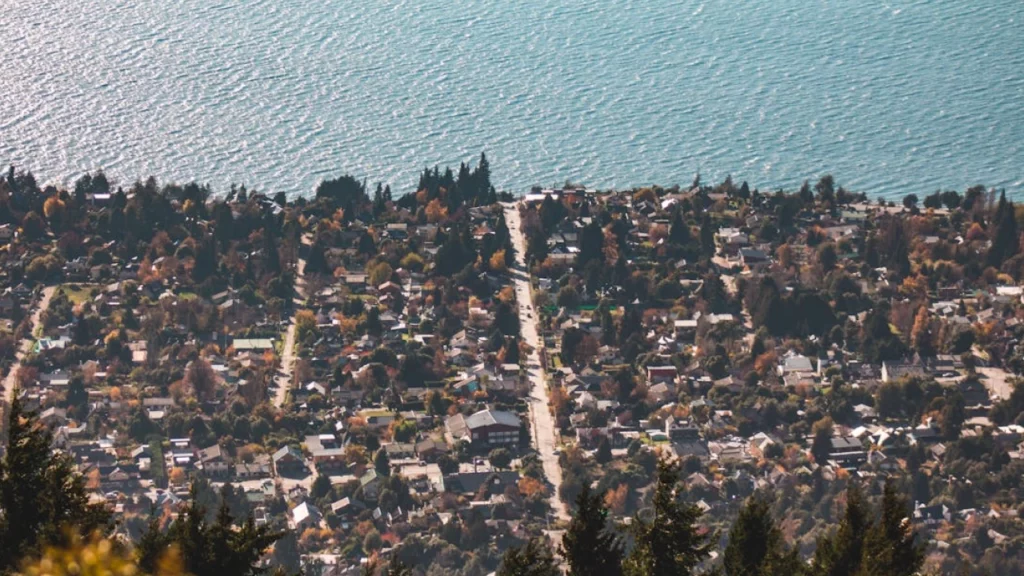 Visão panorâmica de Bariloche, mostrando a cidade cercada por árvores e o lago Nahuel Huapi ao fundo.