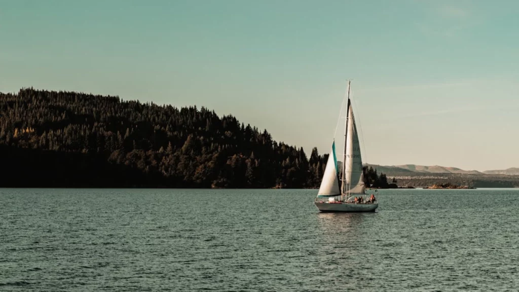 Veleiro navegando pelo Lago Nahuel Huapi, com colinas arborizadas ao fundo e céu claro.