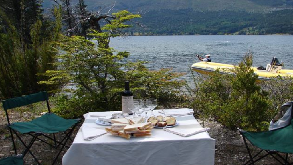 Mesa posta com sanduíches e vinho em clareira de bosque, às margens de um lago em Bariloche.