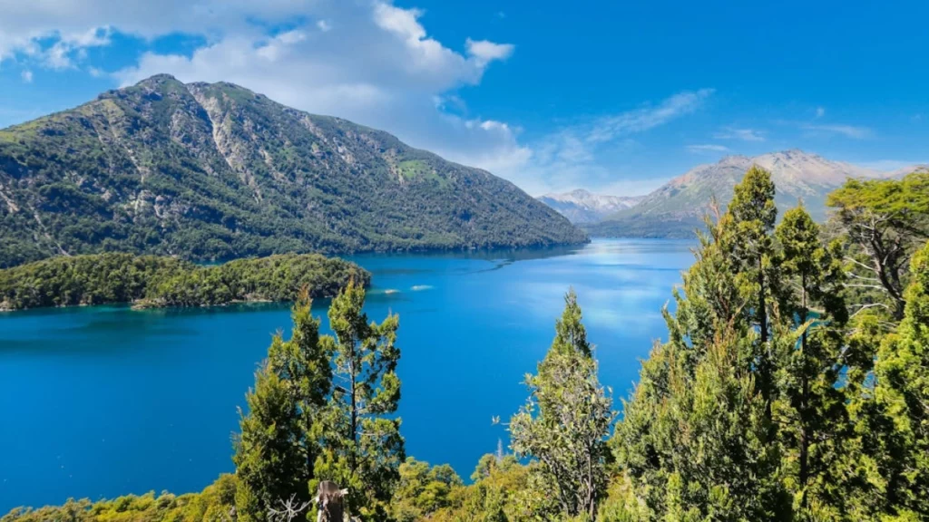 Paisagem deslumbrante de Bariloche, com um lago azul-turquesa cercado por montanhas e árvores exuberantes.