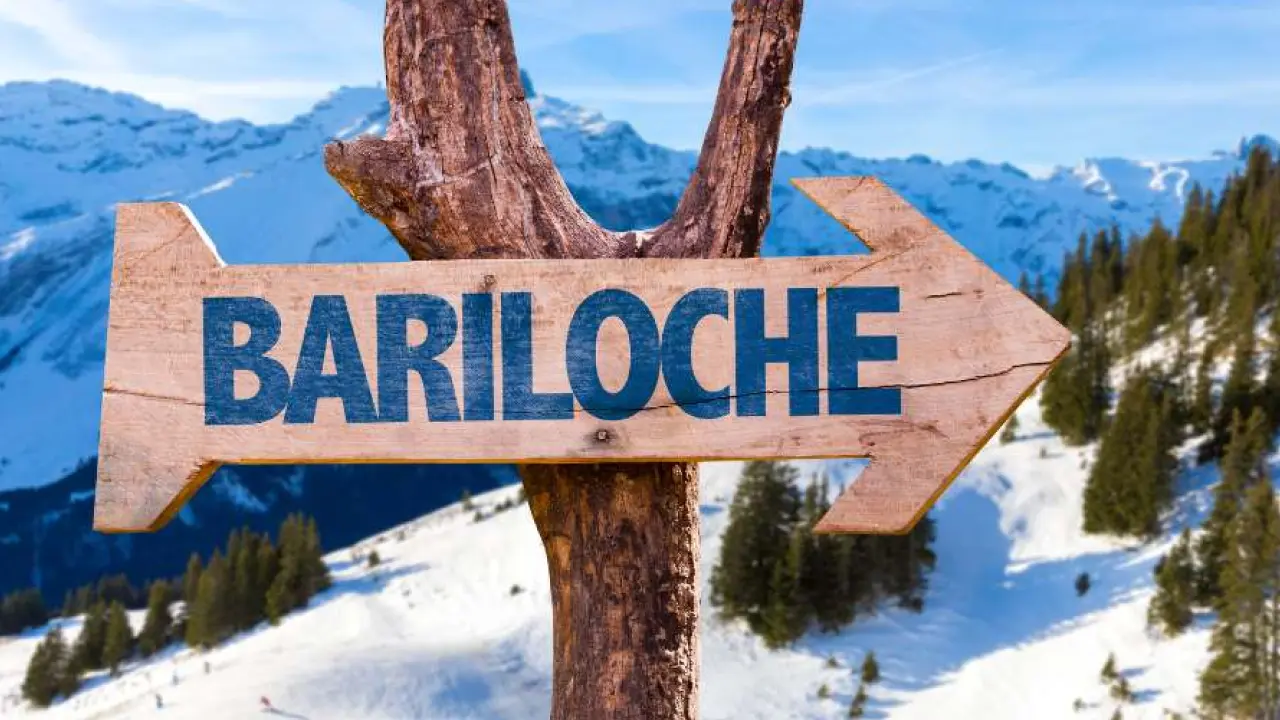 Placa de madeira com a palavra “Bariloche” apontando para a montanha nevada.