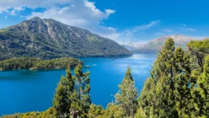 Paisagem deslumbrante de Bariloche, com um lago azul-turquesa cercado por montanhas e árvores exuberantes.