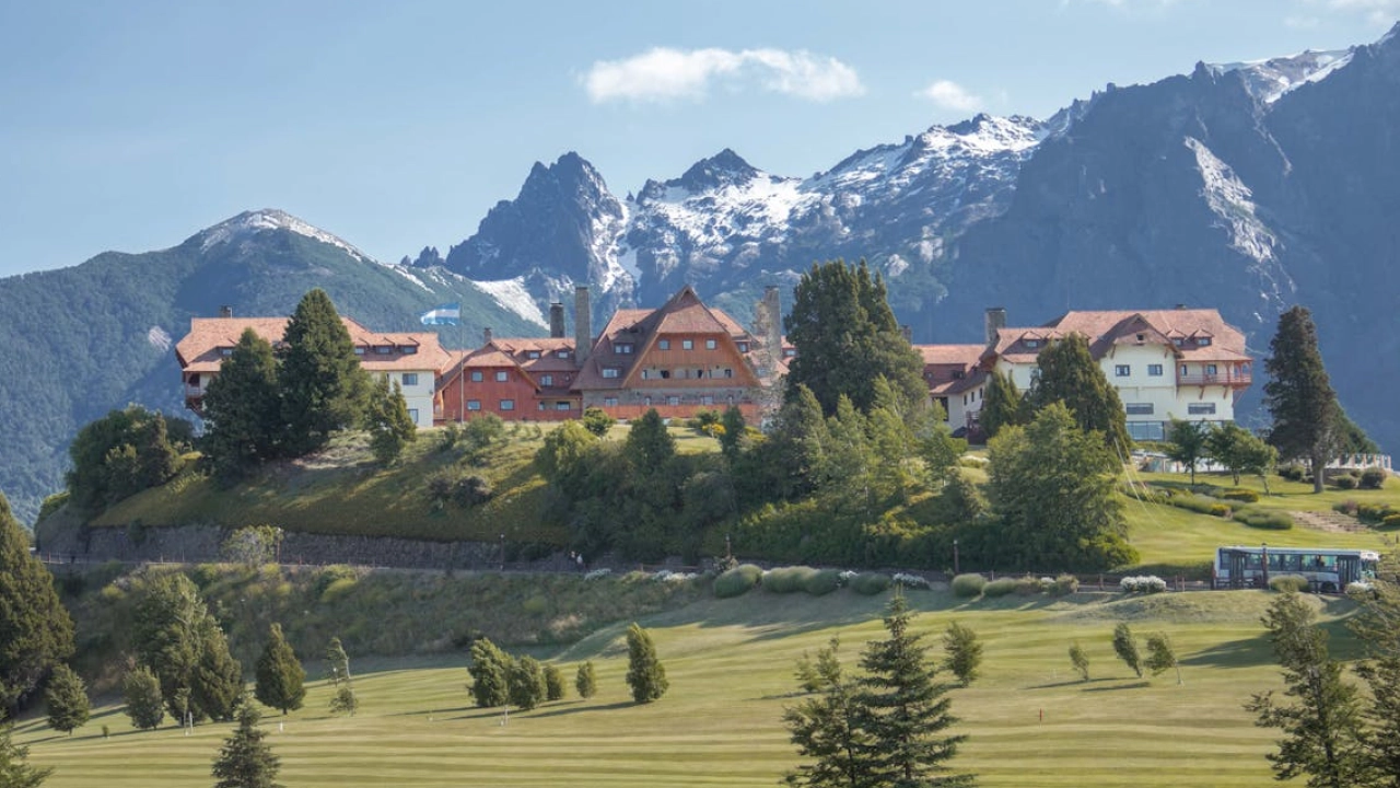 Edificação icônica em Bariloche, cercada por montanhas nevadas e vegetação, com arquitetura em estilo alpino.