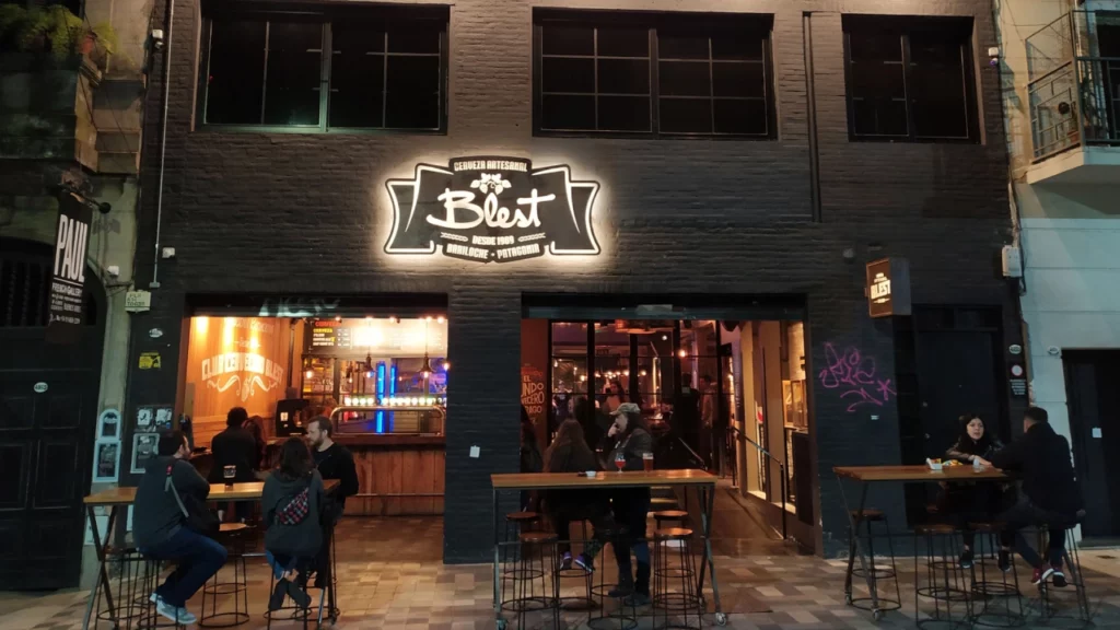 Fachada do Club Cervecero Blest em Bariloche, com clientes sentados nas mesas externas à noite, desfrutando de cerveja artesanal.