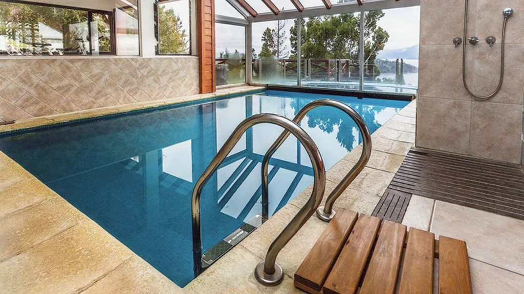 Piscina coberta com vista para o lago e árvores, decorada com azulejos e grandes janelas de vidro que permitem a entrada de luz natural, criando um ambiente relaxante.