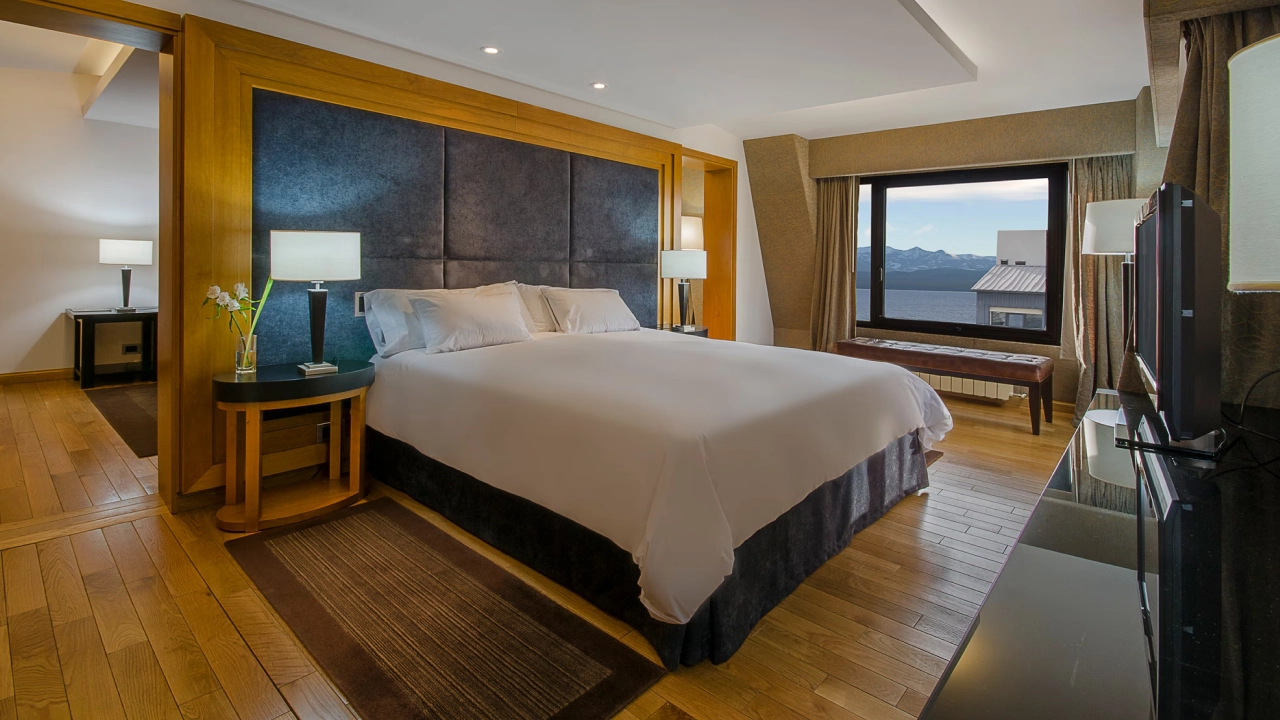 Suíte elegante con cama king-size y amplia janela con vista al deslumbrante Lago Nahuel Huapi, ideal para momentos de relax.