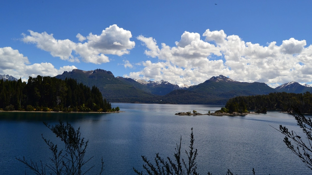 Panorama do Lago Nahuel Huapi em um dia ensolarado, cercado por montanhas e florestas exuberantes em Bariloche.