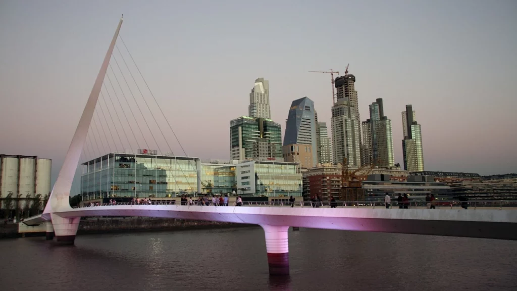 Ponte de la Mujer iluminada ao entardecer em Puerto Madero, Buenos Aires, com arranha-céus modernos ao fundo, destacando a arquitetura contemporânea da cidade.