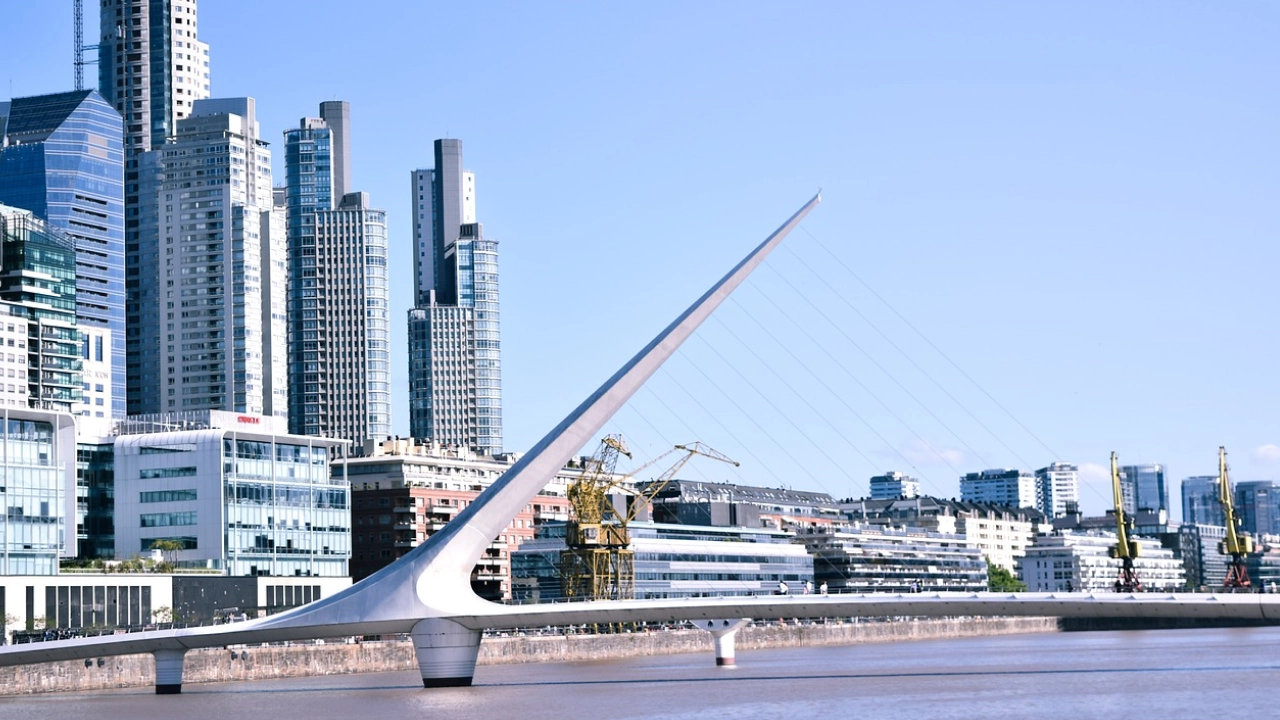 Vista da moderna Puente de la Mujer em Puerto Madero, Buenos Aires, com arranha-céus imponentes ao fundo e o céu azul completando a paisagem urbana da capital argentina.