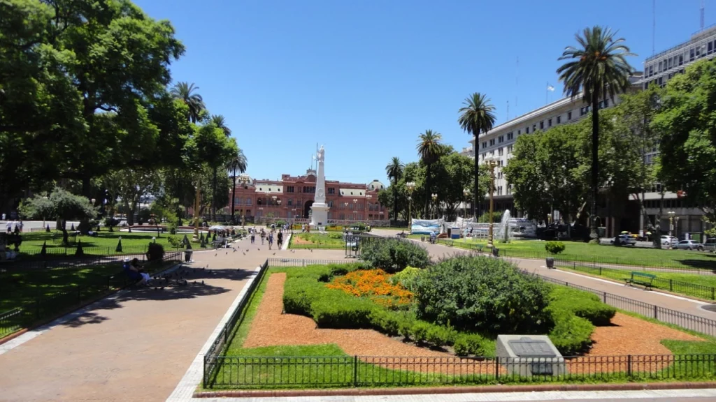 Vista da Plaza de Mayo em Buenos Aires, com jardins bem cuidados, palmeiras altas e a icônica Casa Rosada ao fundo