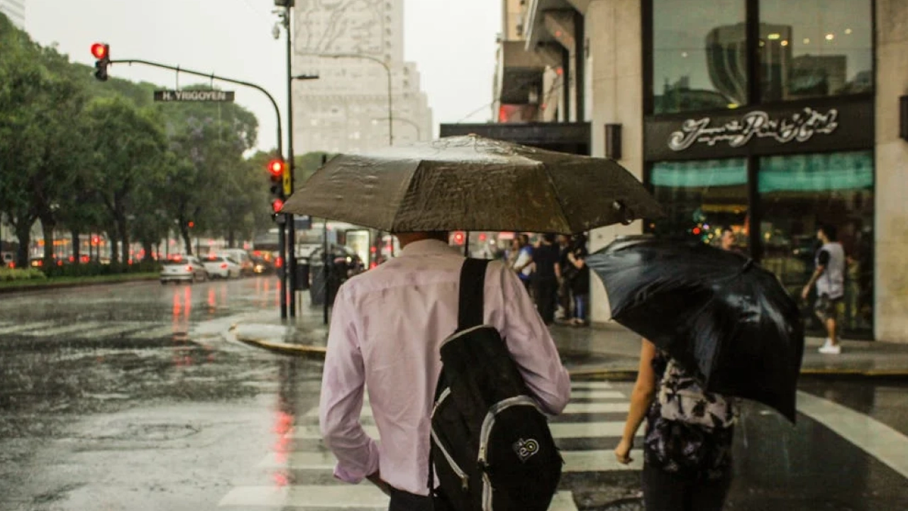 Pessoas caminhando sob chuva com guarda-chuvas em Buenos Aires, mostrando a imprevisibilidade do clima na cidade e a importância de se preparar para mudanças no tempo.