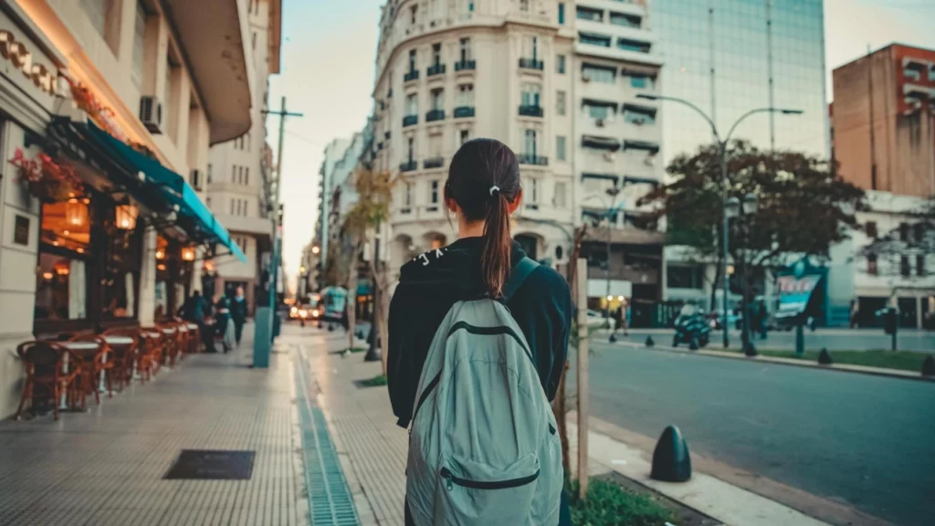 Jovem com mochila caminhando por uma rua charmosa de Buenos Aires, cercada por prédios históricos e restaurantes.