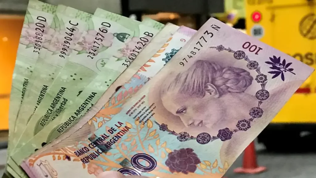 Un primer plano de billetes de 100 pesos argentinos, mostrando el retrato de Eva Perón y detalles florales en los billetes.
