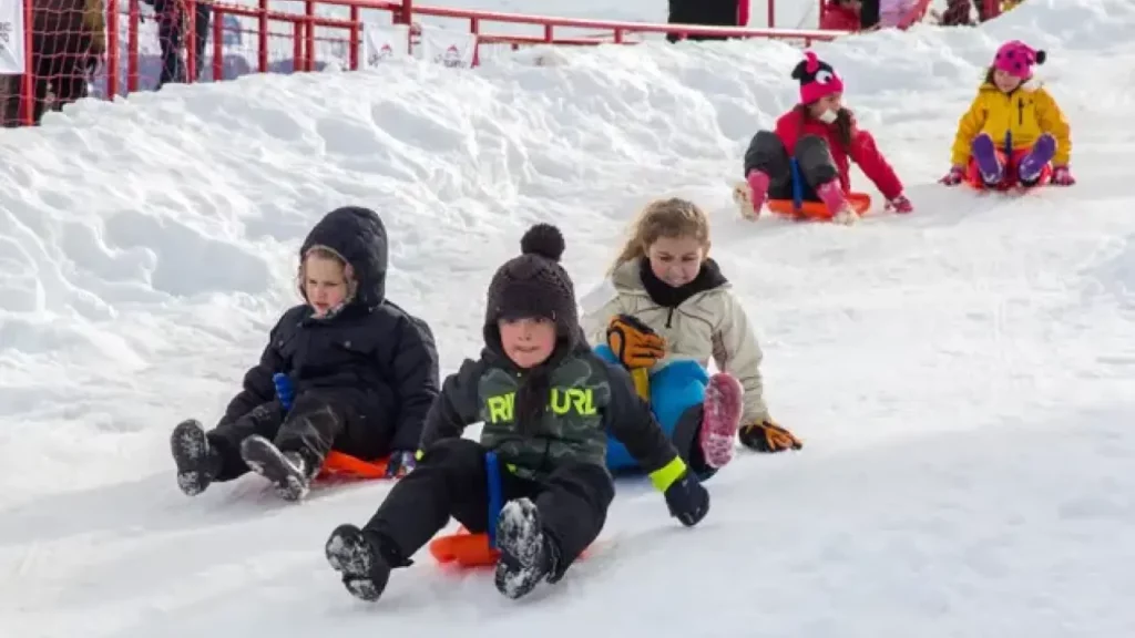 Niños jugando en la nieve, deslizándose en trineos sobre una pista de nieve, disfrutando de un día de invierno.