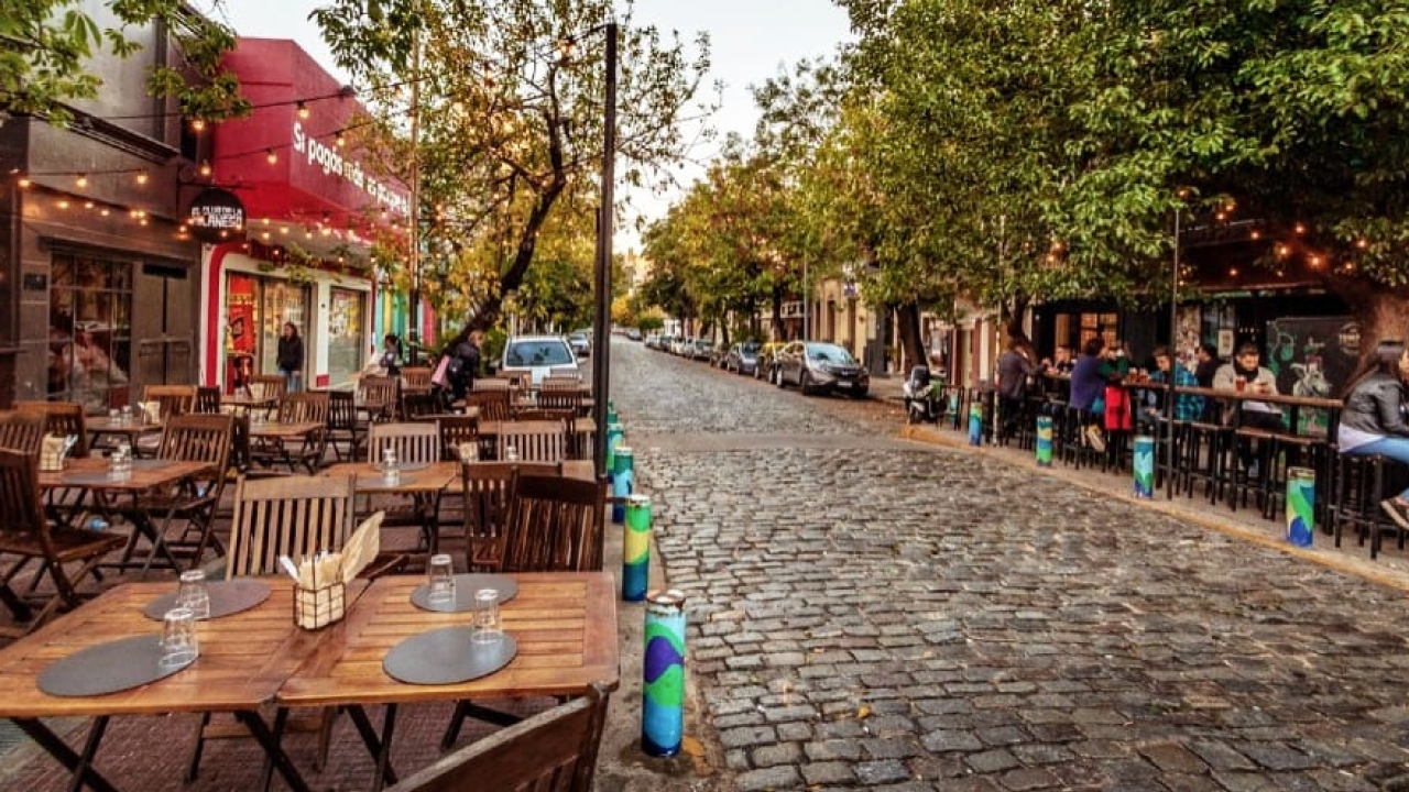 Mesas ao ar livre em rua de paralelepípedos de Palermo Soho, cafés e bares iluminados.